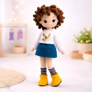 Boneca cacheadinha em amigurumi com suéter branco bordado, saia azul e botinhas amarelas
