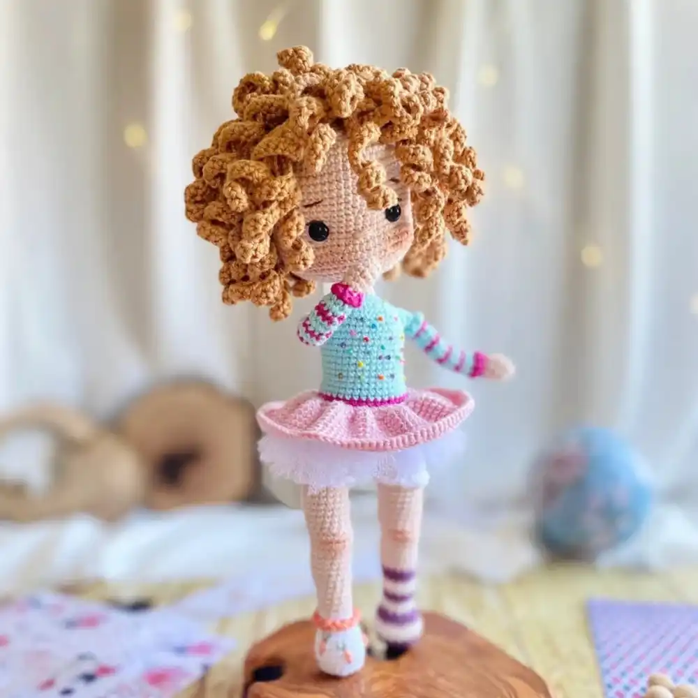 Boneca bailarina em amigurumi com cabelos cacheados caramelo, blusa azul e saia tutu rosa