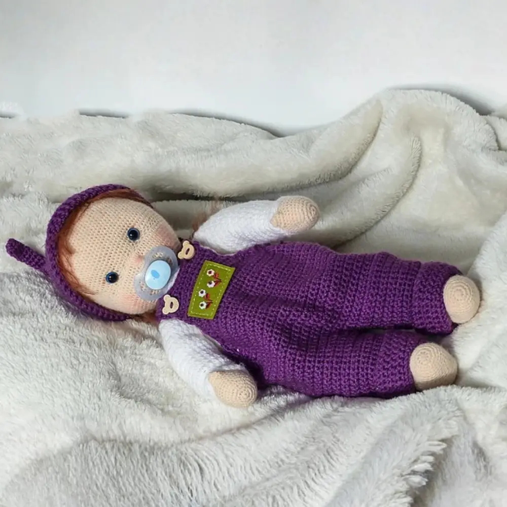 Boneca bebê em amigurumi com chupeta, gorrinho roxo, blusa branca e jardineira roxa
