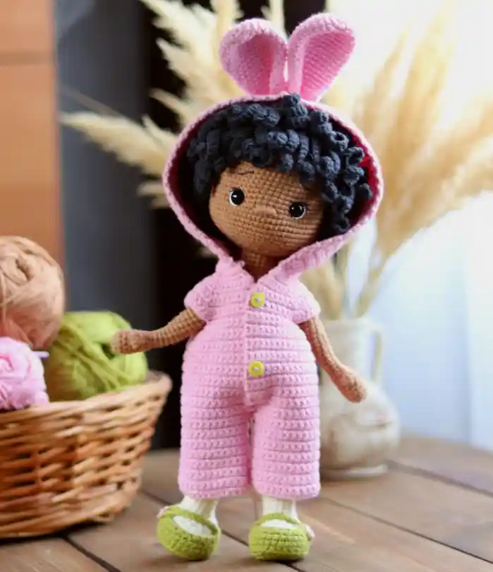 Boneca coelhinha em amigurumi com cabelos cacheados, capuz de orelhas e macacão rosa
