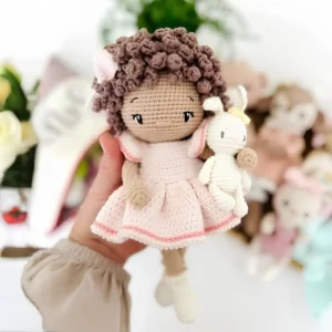 Boneca em amigurumi com cabelos castanhos cacheados, vestido rosa-claro e pequeno coelhinho branco