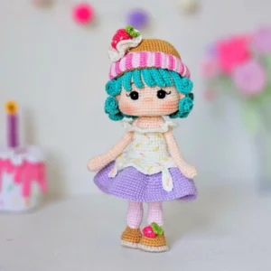 Boneca em amigurumi com cabelo azul-turquesa, touca de morango, saia lilás e sapatinhos decorados