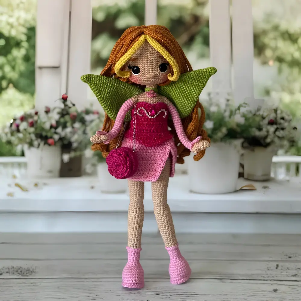 Boneca fada em amigurumi com cabelos castanhos, vestido rosa, asas verdes e botas rosa