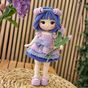 Boneca em amigurumi com cabelos roxos, vestido lilás e rosa e ramos de flores lilás