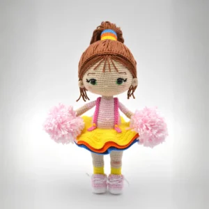 Boneca líder de torcida em amigurumi com saia amarela, roupa rosa e dois pompons rosa