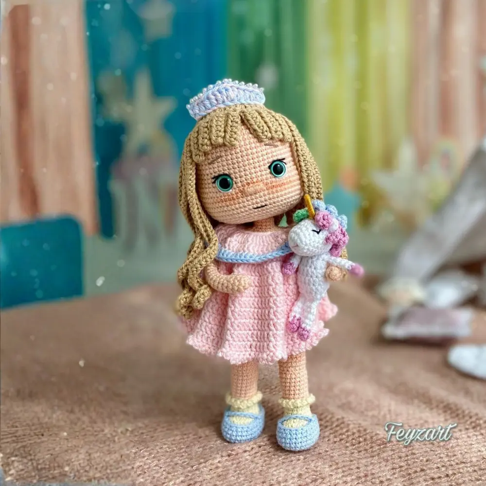 Boneca princesa em amigurumi com cabelos longos, vestido rosa, tiara e pequeno unicórnio branco