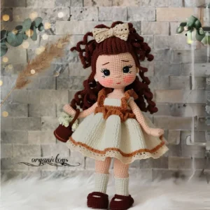 Boneca em amigurumi com cabelos cacheados, vestido creme, laço e bolsinha marrom