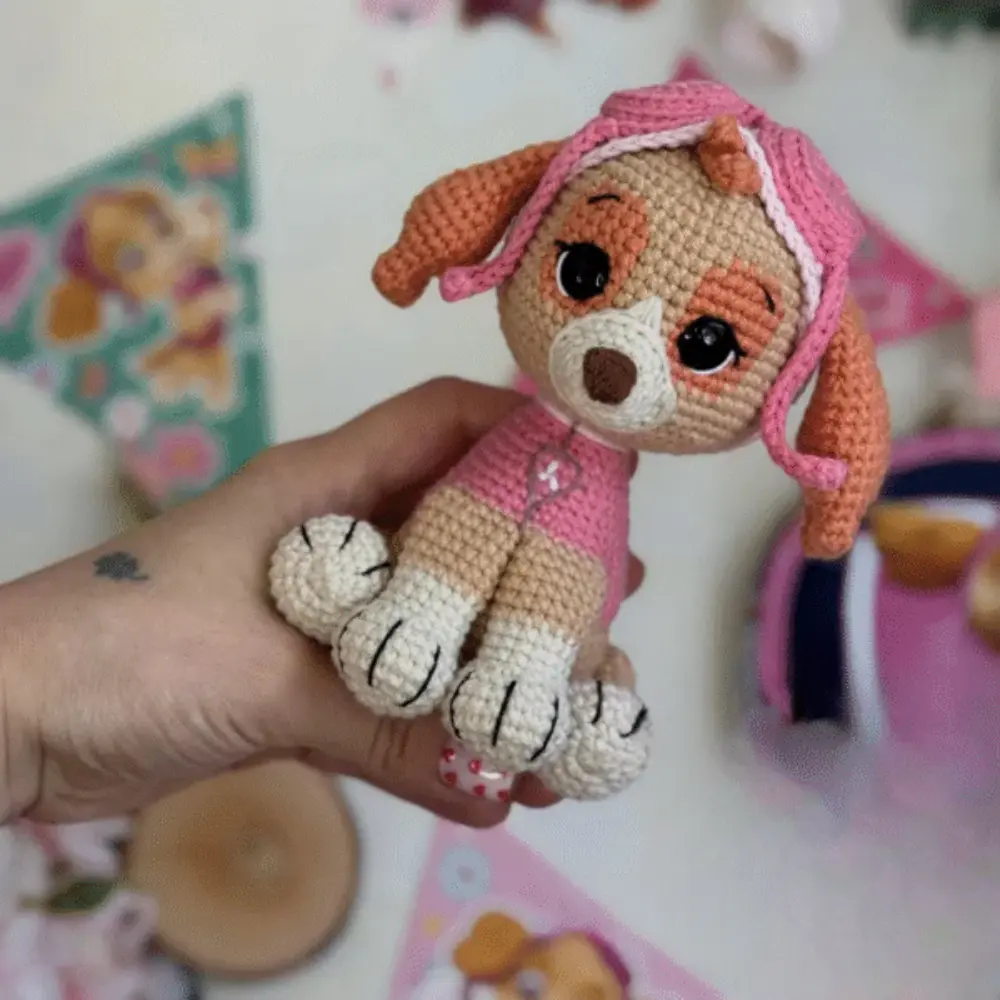 Cachorrinha em amigurumi bege com roupa rosa, orelhas caramelo e gorro de aviadora