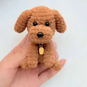 Cachorrinho marrom em amigurumi com orelhas caídas, olhos pretos e coleira com medalhinha