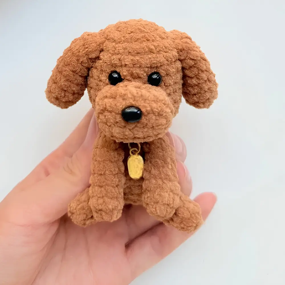 Cachorrinho marrom em amigurumi com orelhas caídas, olhos pretos e coleira com medalhinha