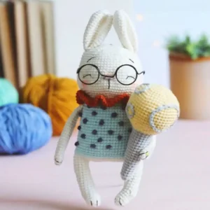 Coelhinho branco em amigurumi com óculos redondos, roupa verde-clara e gola vermelho-alaranjada