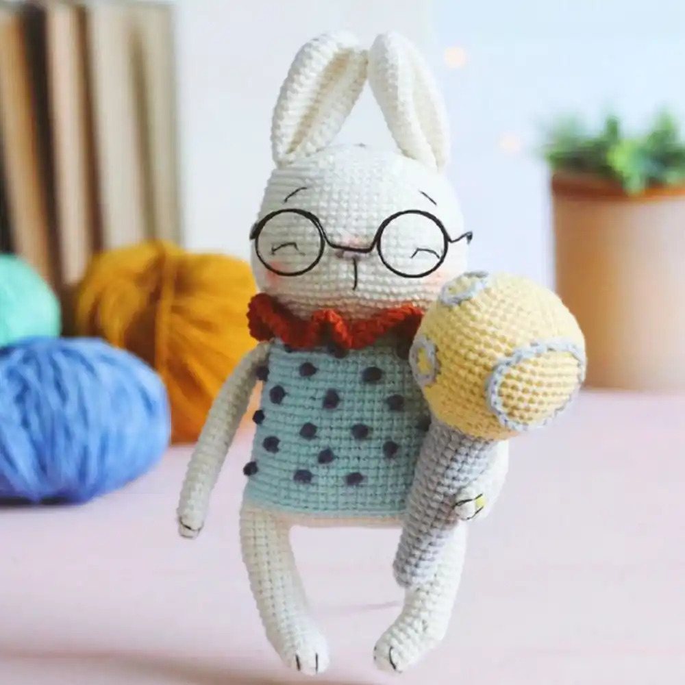 Coelhinho branco em amigurumi com óculos redondos, roupa verde-clara e gola vermelho-alaranjada
