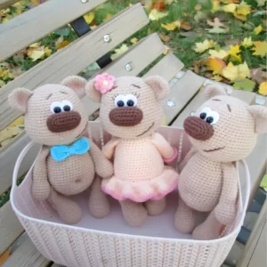 Três ursinhos em amigurumi bege com laço azul, vestido rosa e flor na cabeça