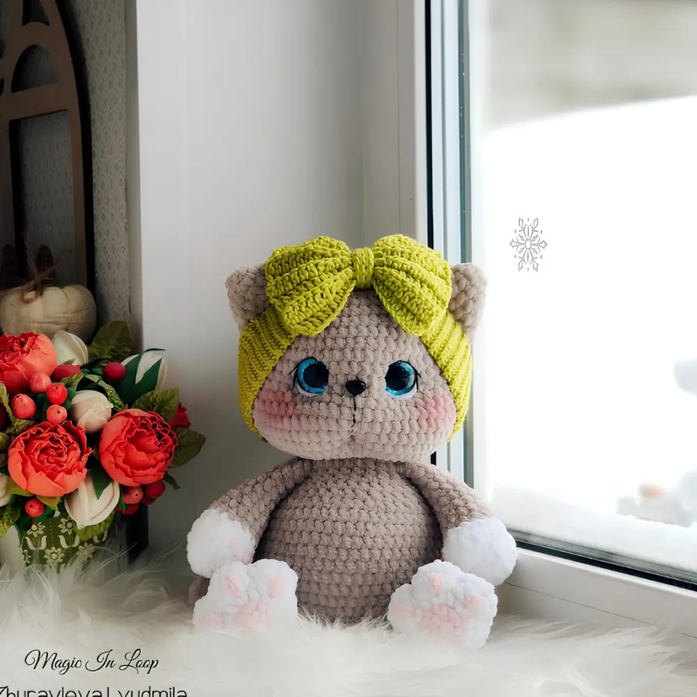 Gatinha cinza em amigurumi com olhos azuis, patas brancas e turbante verde com laço