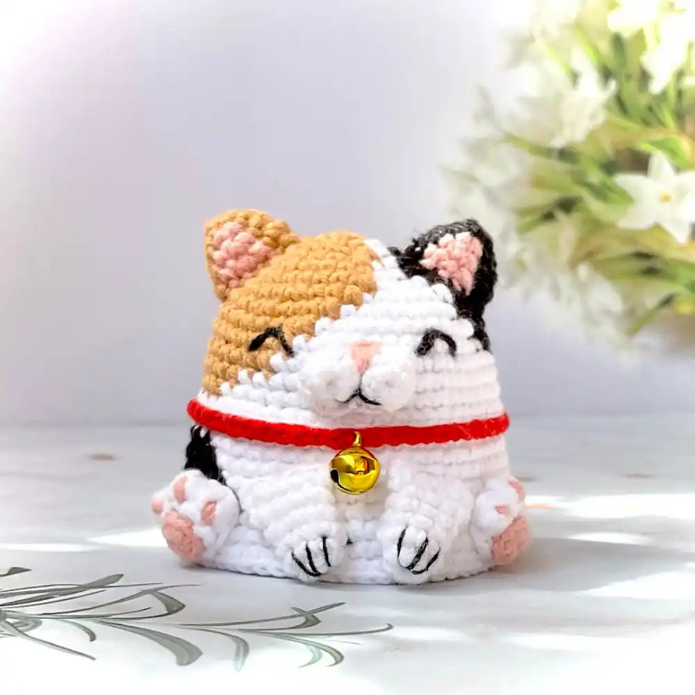 Gatinho tricolor em amigurumi branco, caramelo e preto com coleira vermelha e sino dourado