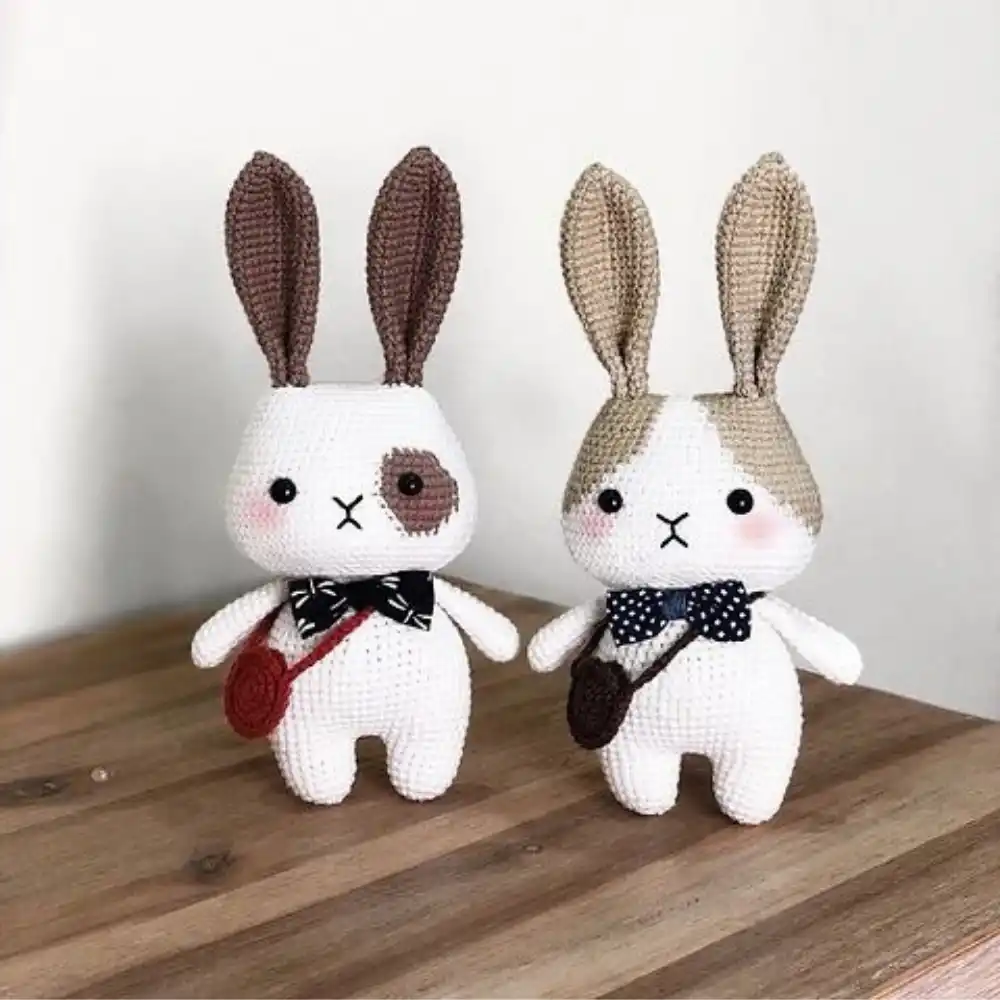 Dois coelhinhos em amigurumi brancos com orelhas longas, gravatas-borboleta e bolsinhas transversais