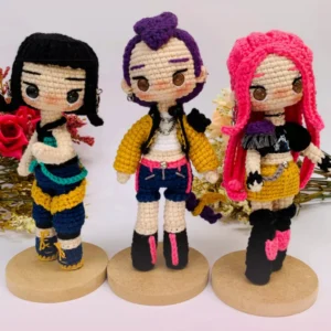 Três bonecas KPop Demon Hunters em amigurumi com cabelos preto, roxo e rosa e roupas coloridas