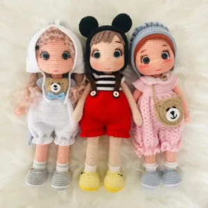 Três bonecas em amigurumi com roupas branca, vermelha e rosa e acessórios variados