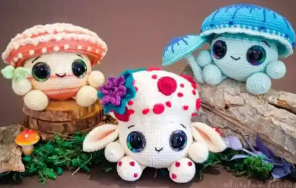 Três cogumelos encantados em amigurumi nas cores laranja, vermelho e azul