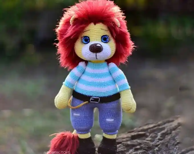 Leãozinho em amigurumi com juba volumosa, blusa listrada e calça azul
