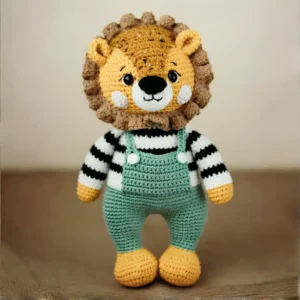 Leãozinho em amigurumi com juba marrom, blusa listrada preta e branca e jardineira verdec