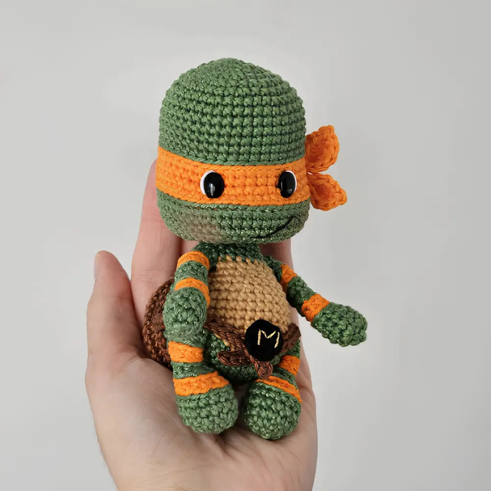 Tartaruga Ninja Michelangelo em amigurumi verde com máscara laranja, casco marrom e cinto com letra M