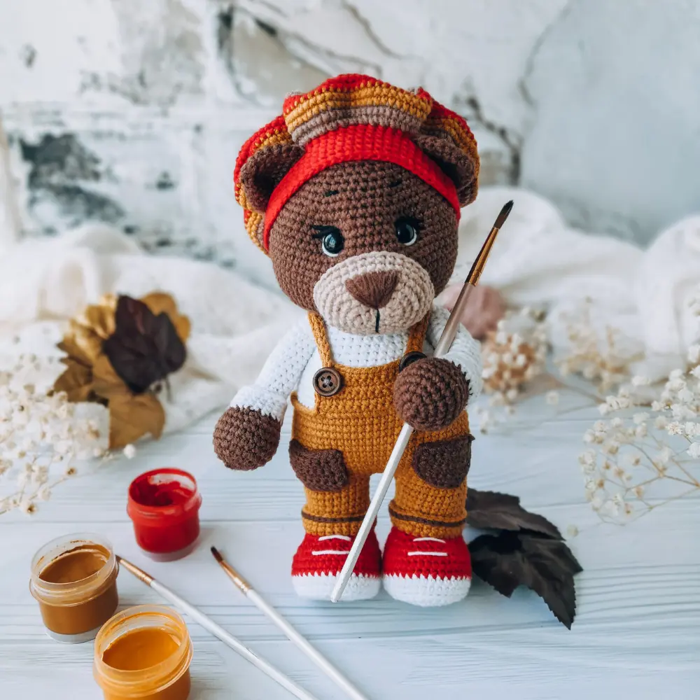 Ursinho marrom em amigurumi com jardineira mostarda, camiseta branca e tênis vermelhos